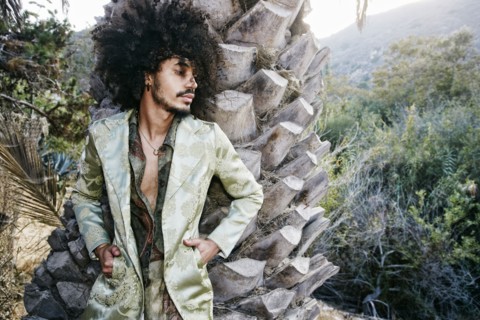 Mixed Race man wearing jacket leaning on tree trunk