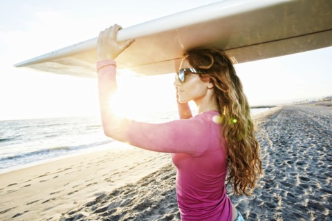 Caucasian woman carrying surfboard on beach
