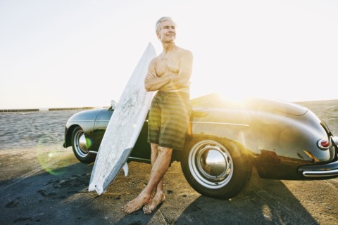 Older Caucasian man on leaning on convertible car with surfboard