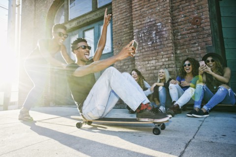 Woman pushing friend sitting on skateboard in city