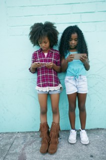 Girls leaning on wall texting on cell phones