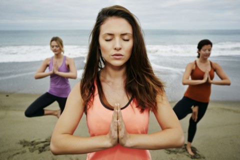 Caucasian women performing yoga on beach