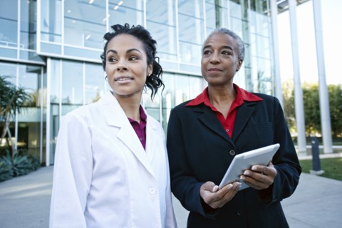 Doctor and administrator outdoors at hospital using digital tablet