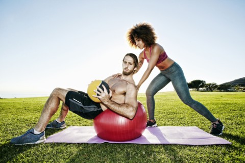 Couple exercising with fitness ball and heavy ball in sunny field