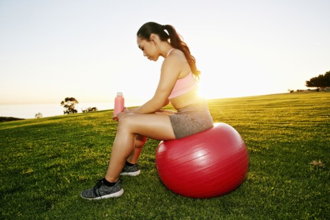 Mixed Race woman resting on fitness ball in sunny field
