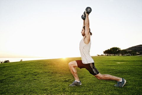 Caucasian man lifting dumbbells in sunny field