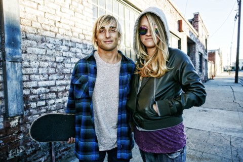 Caucasian couple with skateboard posing on urban sidewalk