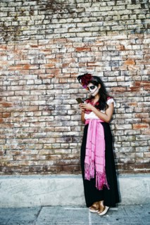 Mixed Race woman on sidewalk wearing skull face paint texting on cell phone