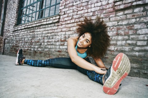 Hispanic woman sitting on sidewalk stretching legs near brick wall
