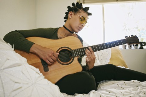 Mixed Race woman sitting on bed playing guitar