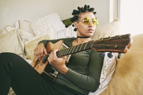 Mixed Race woman sitting on bed playing guitar