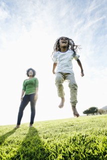 Mixed race mother watching daughter jumping in the grass