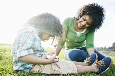 Mixed race mother watching son use cell phone in grass