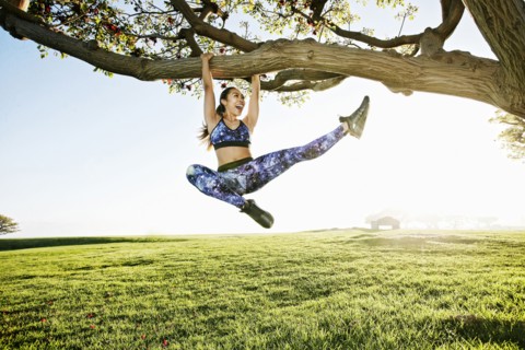 Happy mixed race woman hanging on tree branch