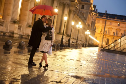 Caucasian couple kissing in rain at night at the Louvre