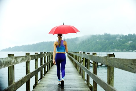 Caucasian woman in sportswear with red umbrella on pier