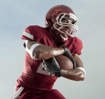 Grimacing Black football player carrying football