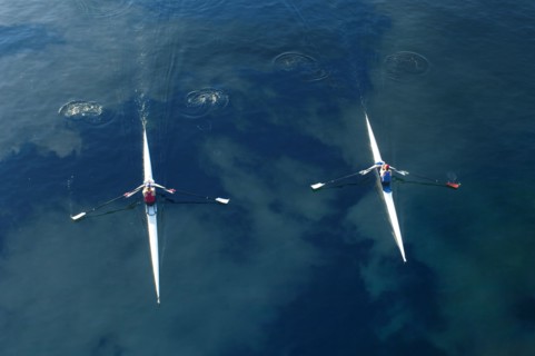 People rowing sculling boats on river