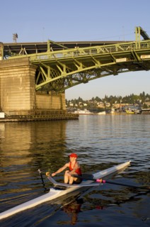 Person rowing sculling boat on river under bridge