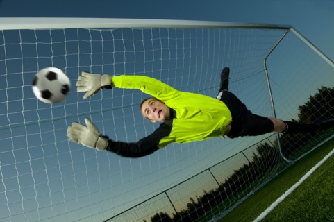 Caucasian soccer goalie jumping in mid-air catching ball