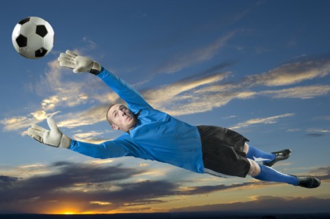 Caucasian soccer goalie jumping in mid-air catching ball