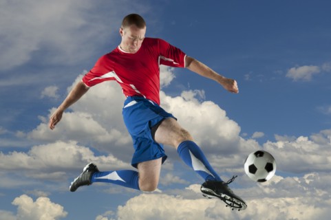 Caucasian soccer player jumping in mid-air kicking ball