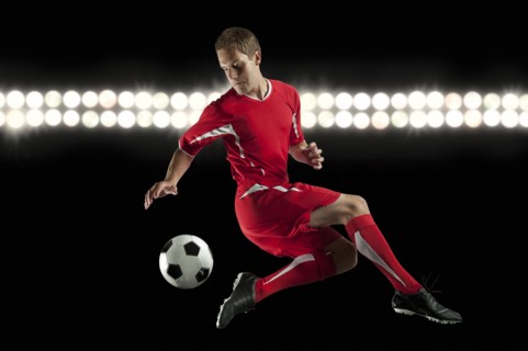 Soccer player jumping in mid-air kicking ball at night