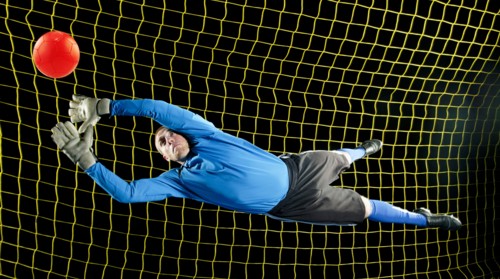 Caucasian soccer goalie jumping in mid-air catching ball at night