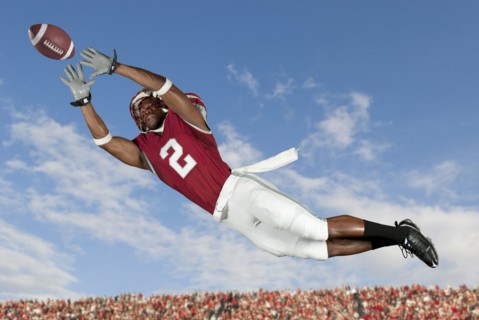 Black football player catching football in mid-air