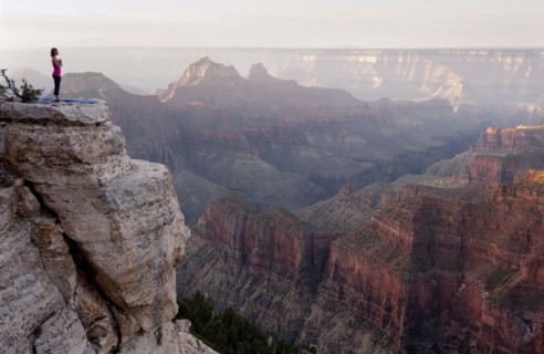 Caucasian woman practicing yoga on cliff near canyon