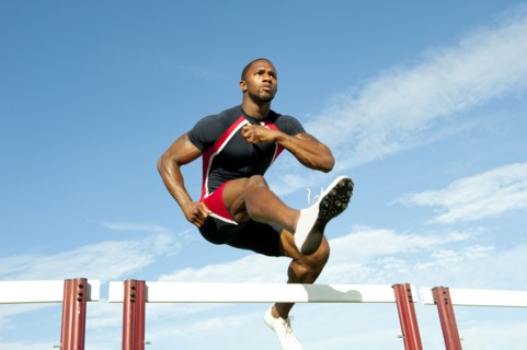Black runner jumping hurdles in track race