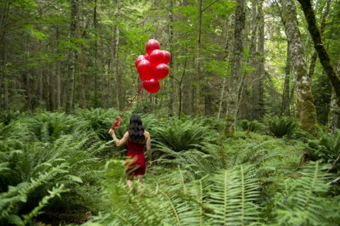 Korean woman holding red balloons in lush forest