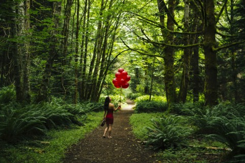 Korean woman holding red balloons in lush forest