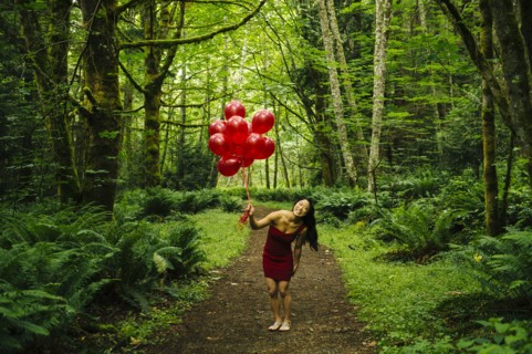 Korean woman holding red balloons in lush forest