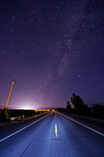 Paved road under starry night sky illuminated by headlights