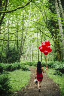 Korean woman holding red balloons in lush forest