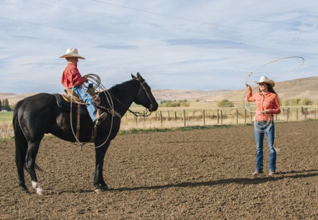 Caucasian woman teaching boy to use lasso on ranch