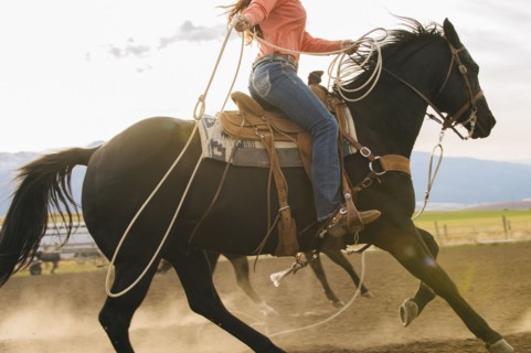 Caucasian woman on horse throwing lasso at rodeo