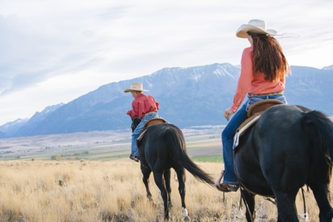 Caucasian mother and son riding horses in grassy field