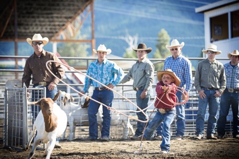 Cowboys teaching boy to lasso goat at rodeo