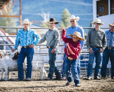 Cowboys watching boy throw lasso in rodeo