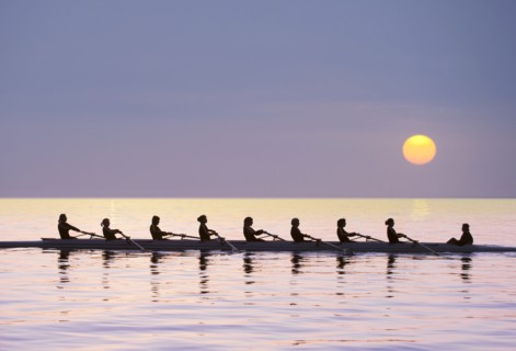 Silhouette of rowing team practicing on still lake