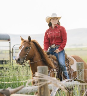 Caucasian cowgirl riding horse on ranch