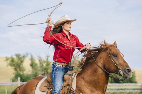 Caucasian cowgirl throwing lasso on horseback