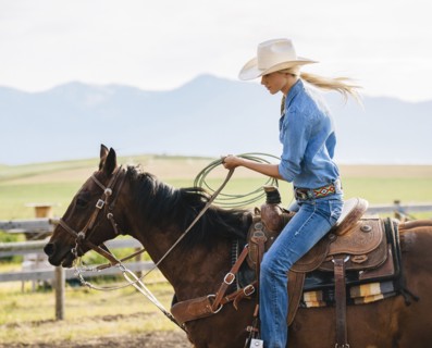 Caucasian cowgirl holding lasso on horseback