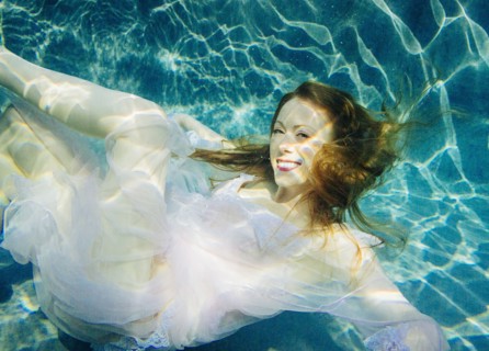 Caucasian woman wearing dress swimming underwater