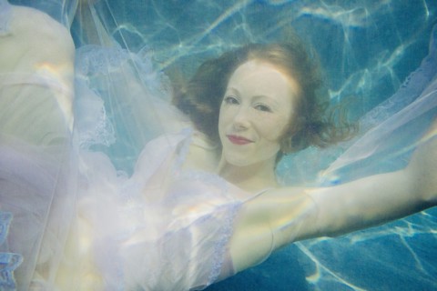 Caucasian woman wearing dress swimming underwater