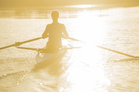 Caucasian man rowing on river at sunset