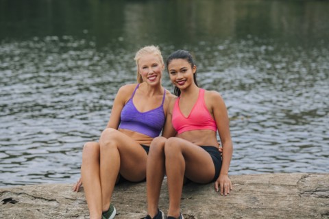 Portrait of smiling women sitting on log near lake