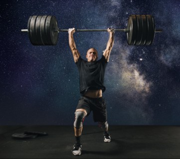 Man lifting heavy barbell against starry sky